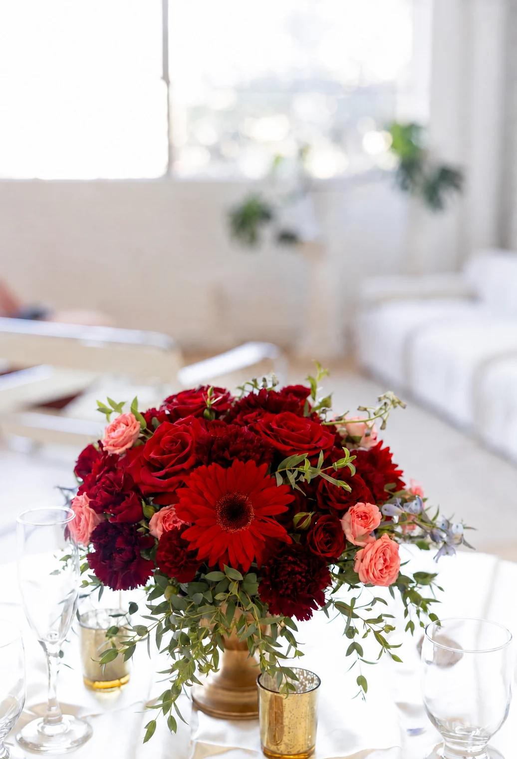 Red rose and gerbera centerpiece in a gold vase with gold votives