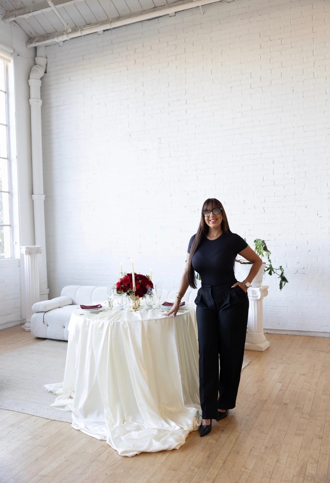 Patricia Perez beside an ivory draped table set with red florals and gold candlesticks
