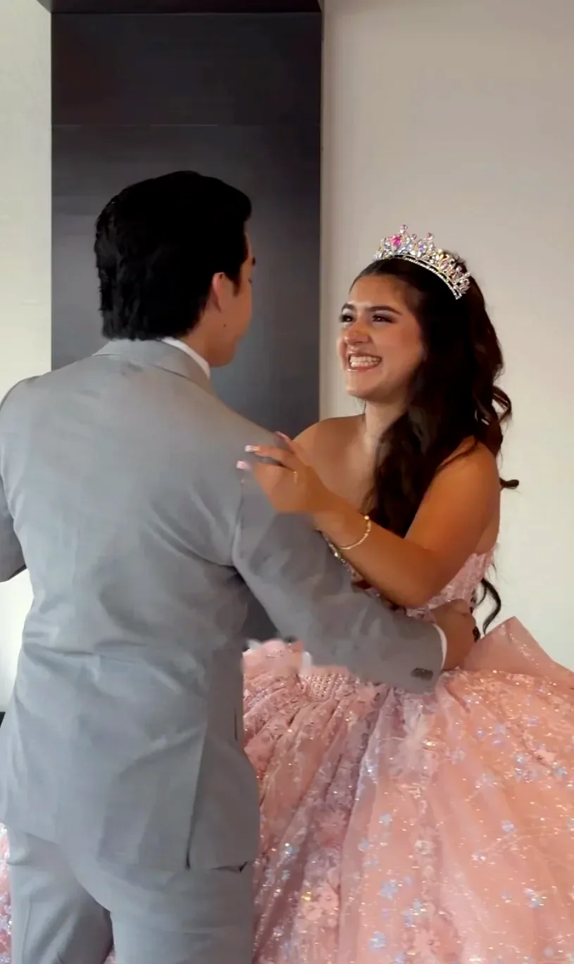 Quinceañera in a pink gown and tiara dancing with her brother